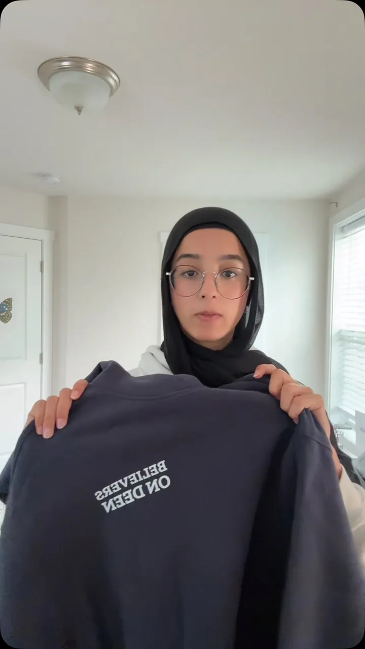 Cover frame from @maryams_png's reel, holding the United Ummah Hoodie